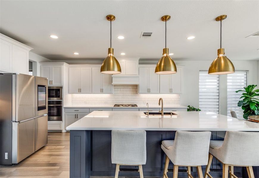 Kitchen featuring stainless steel appliances, white cabinetry, decorative light fixtures, backsplash, and a center island with sink