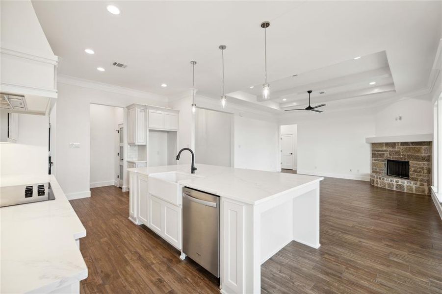 Kitchen featuring a fireplace, white cabinetry, an island with sink, ceiling fan, and dark wood-type flooring