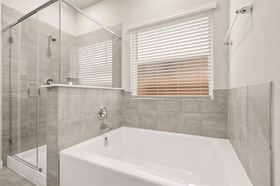 An additional view of the Primary Bath Oasis featuring a glass encased walk-in shower with tile surround, separate soaking tub, water closet for added privacy and oversized window to bring in tons of natural light.