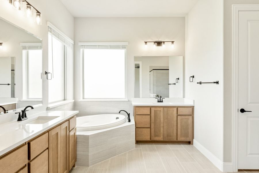 Master bathroom with dual vanities, corner soaking tub, wood cabinets, and white countertops on light tile floors Master bathroom with dual vanities, corner soaking tub, wood cabinets, and white countertops on light tile floors
