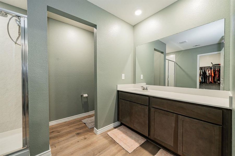 Full bathroom with a spacious closet, light wood-style flooring, vanity, a shower stall, and a textured wall Full bathroom with a spacious closet, light wood-style flooring, vanity, a shower stall, and a textured wall