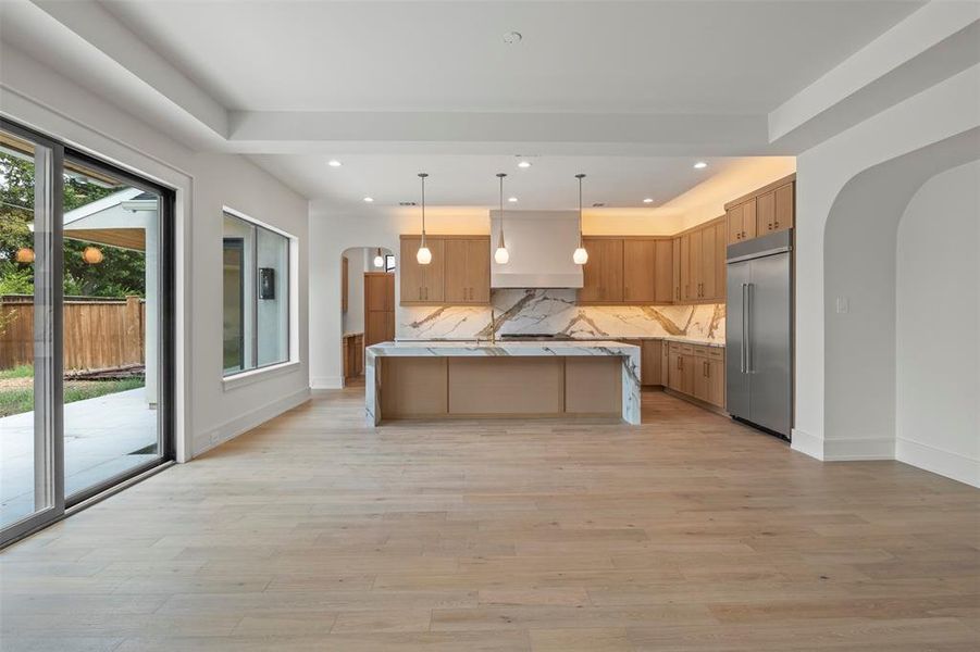 Kitchen featuring arched walkways, tasteful backsplash, decorative light fixtures, built in fridge, and light stone countertops Kitchen featuring arched walkways, tasteful backsplash, decorative light fixtures, built in fridge, and light stone countertops