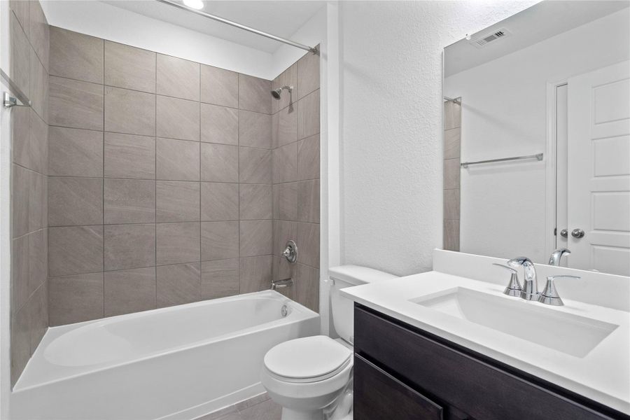 The secondary bathroom showcases tile flooring, a bath/shower combo with Daltile tile surround, a vanity with a stunning light countertop, a stylish mirror, sleek fixtures, and contemporary finishes throughout.