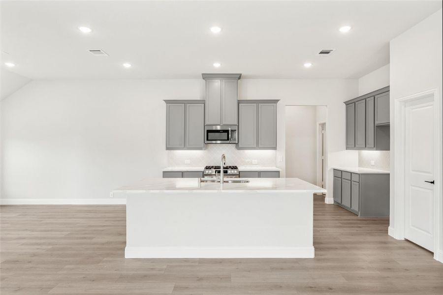 Kitchen with large white island, gray cabinets, stainless steel appliances, and light wood floors Kitchen with large white island, gray cabinets, stainless steel appliances, and light wood floors