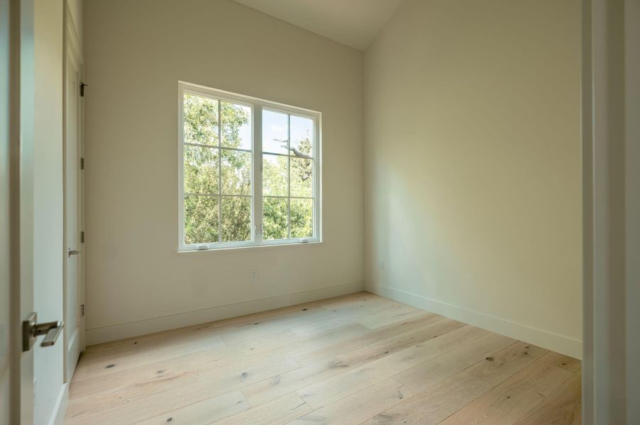 Sunlight streams through the large window onto light hardwood flooring beneath a vaulted ceiling. Sunlight streams through the large window onto light hardwood flooring beneath a vaulted ceiling.