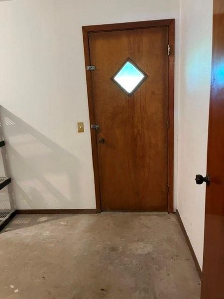 Wood-finish door featuring a diamond-shaped window, set within a white wall, above a concrete floor Wood-finish door featuring a diamond-shaped window, set within a white wall, above a concrete floor