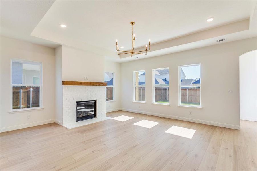 Unfurnished living room with light hardwood / wood-style floors, a raised ceiling, a fireplace, and an inviting chandelier