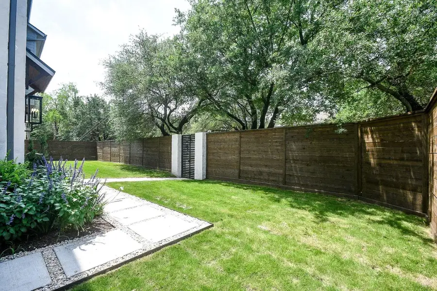 Large yard with Cavalier Zoysia Sod, Under Bed Sprinklers, French Drain System, bordered by a wooden fence for privacy. The space features a stone pathway and mature trees providing shade, creating a serene outdoor area for relaxation or entertaining. Space for future pool