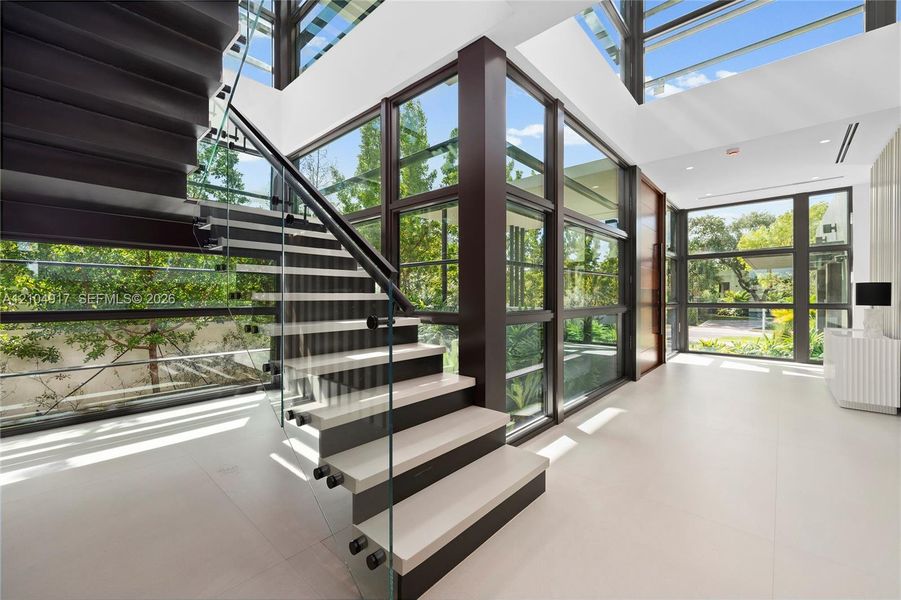 Modern staircase with glass railing, dark wood risers, light-toned treads, and large format floor tiling