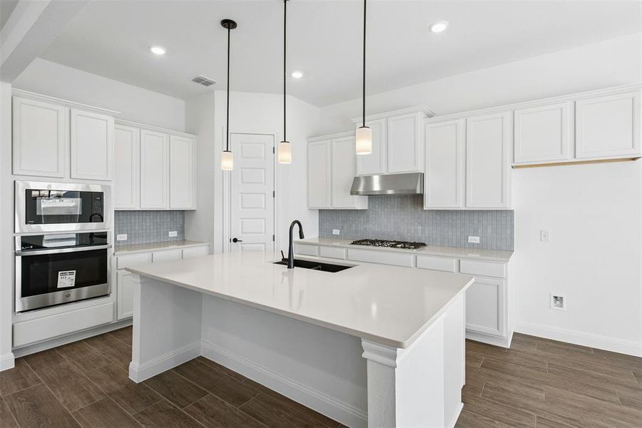 Modern kitchen featuring a large central island with a solid surface countertop, white shaker cabinetry, stainless steel appliances, and wood-finish flooring