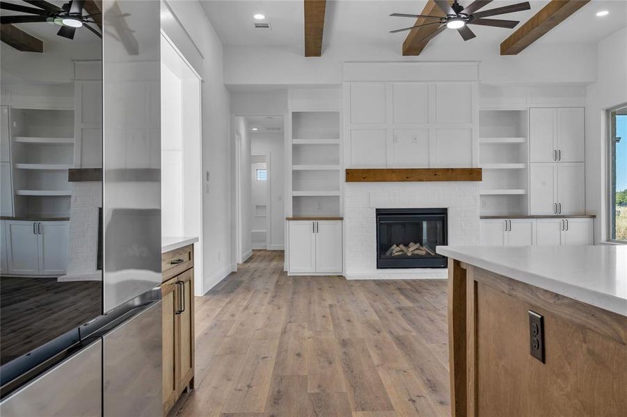 Unfurnished living room with a ceiling fan, a fireplace, beam ceiling, light wood-style floors, and built in features