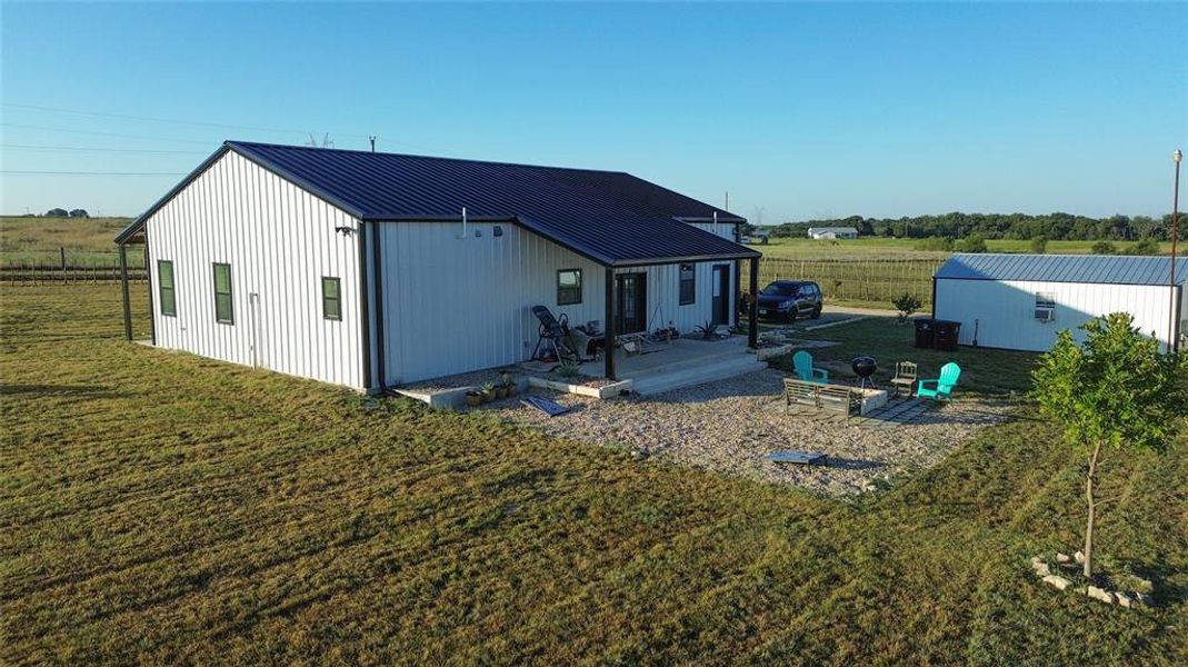 Rear view of property with a rural view, a yard, an outbuilding, a patio area, and a fire pit Rear view of property with a rural view, a yard, an outbuilding, a patio area, and a fire pit