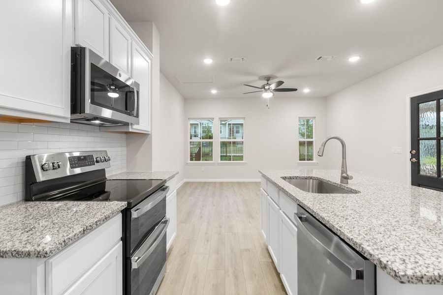 The kitchen features light-colored countertops, white cabinetry, and stainless steel appliances, including an oven, microwave, and dishwasher