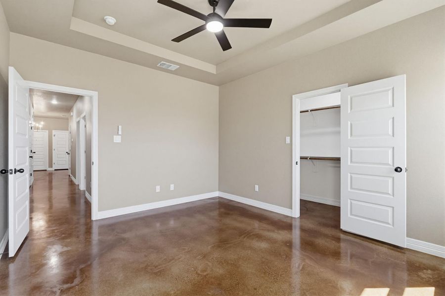 Unfurnished bedroom featuring concrete flooring, a spacious closet, a tray ceiling, and ceiling fan