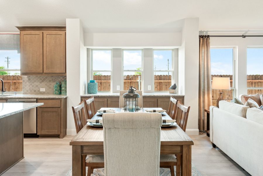 Open-concept dining area with wood table, adjacent kitchen with brown cabinets, and living room with large windows Open-concept dining area with wood table, adjacent kitchen with brown cabinets, and living room with large windows