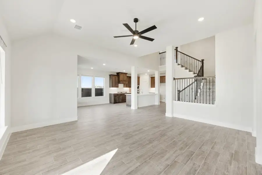 Open living area with vaulted ceiling, ceiling fan, wood-look tile floors, and staircase leading to kitchen