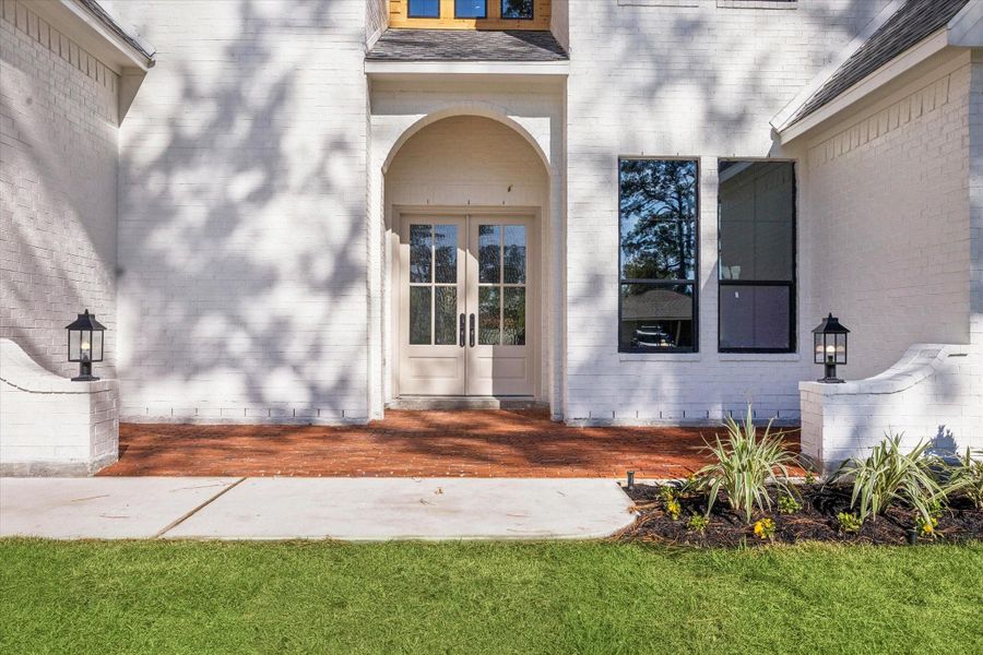 Covered front entry with brick porch, double glass doors, and updated landscaping.