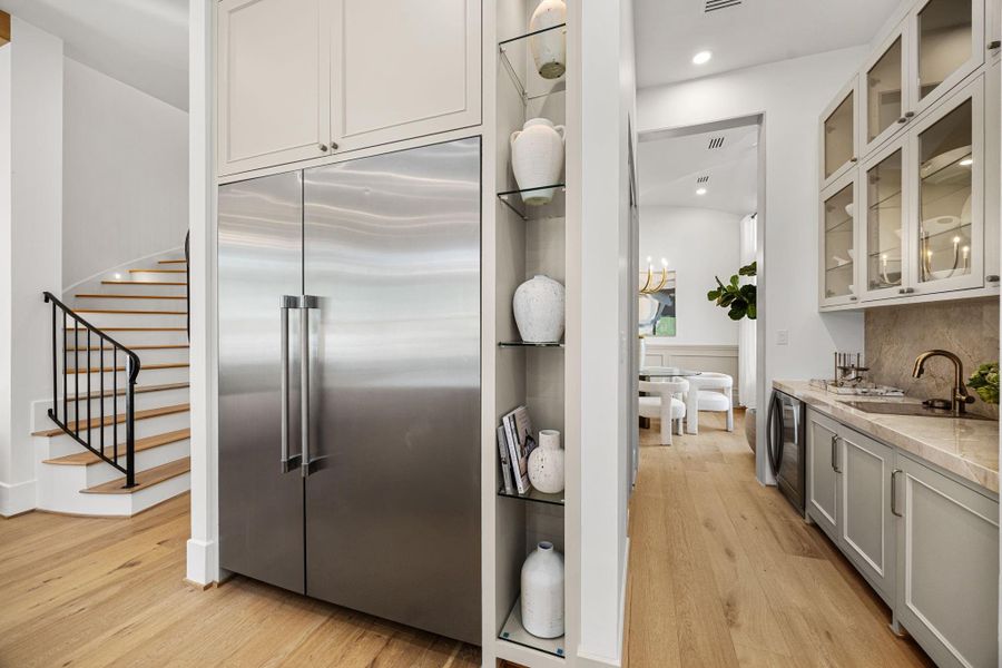 Butler's Pantry features Taj Mahal counters/backsplash, glass-front windows, beverage fridge, wet bar sink w/ glass washer & a walk-in pantry opposite the counter. Butler's Pantry features Taj Mahal counters/backsplash, glass-front windows, beverage fridge, wet bar sink w/ glass washer & a walk-in pantry opposite the counter.