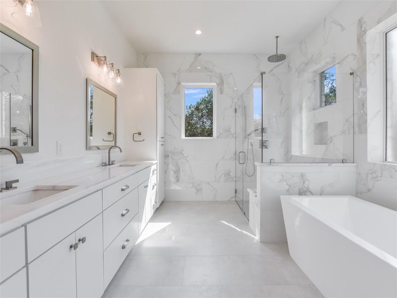 Full bath featuring double vanity, a freestanding bath, a marble finish shower, and a sink