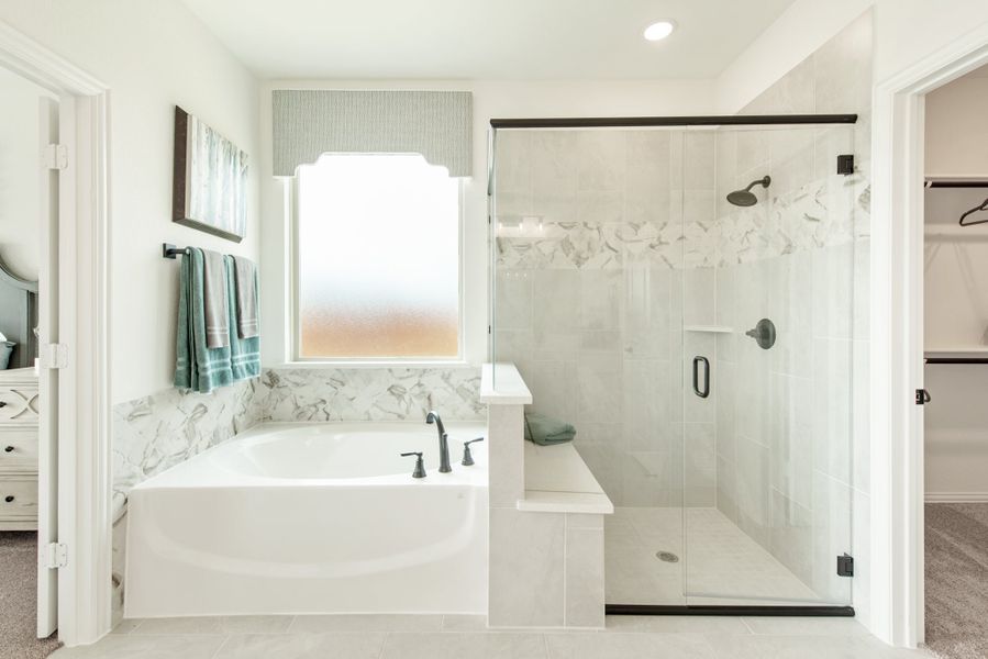 Master bathroom with soaking tub, glass-enclosed shower, marble tile accents, and walk-in closet entry Master bathroom with soaking tub, glass-enclosed shower, marble tile accents, and walk-in closet entry
