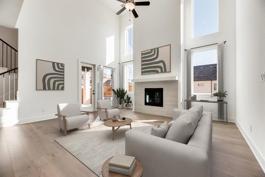 Living area with healthy amount of natural light, a tiled fireplace, light wood-style floors, a towering ceiling, and a ceiling fan