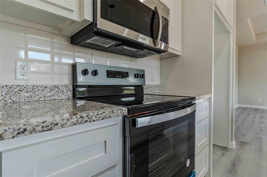 Kitchen with tasteful backsplash, white cabinets, stainless steel appliances, light hardwood / wood-style floors, and light stone countertops