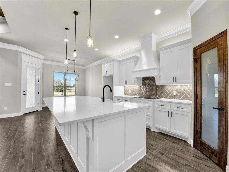 Kitchen featuring pendant lighting, sink, custom range hood, white cabinets, and a center island with sink