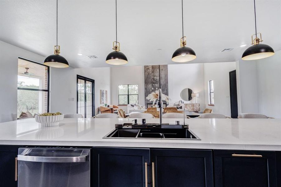 Kitchen island featuring a dual-basin sink with a matte black faucet, integrated stainless steel dishwasher, and dark cabinetry with gold-tone hardware Kitchen island featuring a dual-basin sink with a matte black faucet, integrated stainless steel dishwasher, and dark cabinetry with gold-tone hardware
