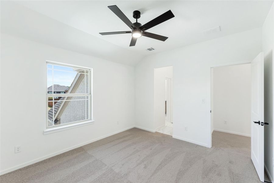 Empty bedroom with beige carpet, black ceiling fan, and a window with neighborhood view