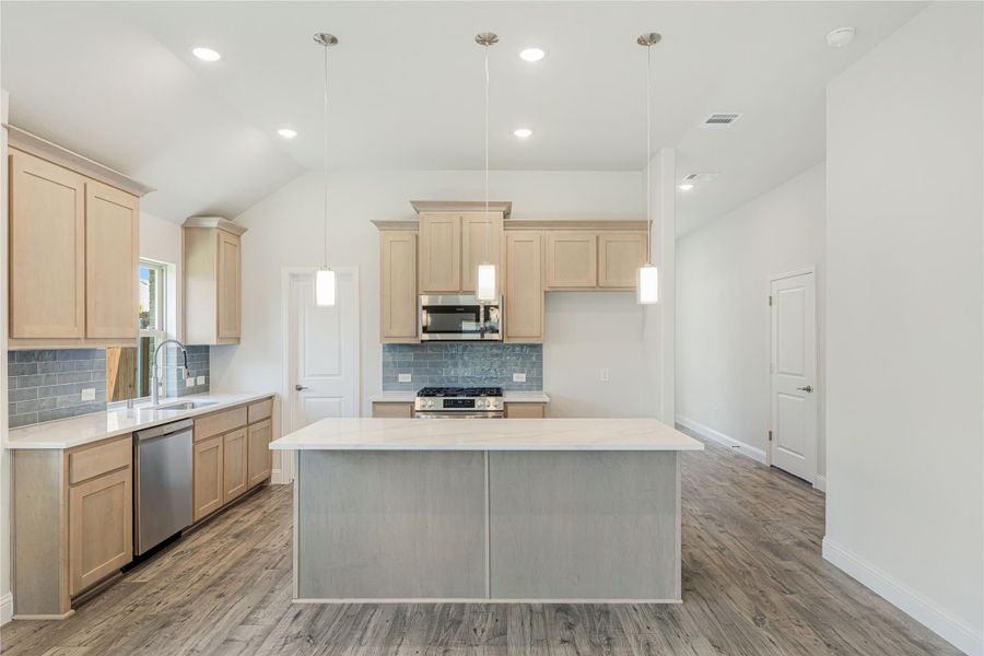 Kitchen with light wood cabinets, center island, stainless steel appliances, and gray tile backsplash on wood-look floors Kitchen with light wood cabinets, center island, stainless steel appliances, and gray tile backsplash on wood-look floors