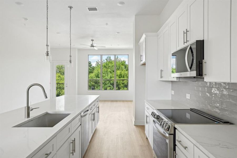 Kitchen featuring appliances with stainless steel finishes, a sink, light wood-style floors, backsplash, and white cabinets