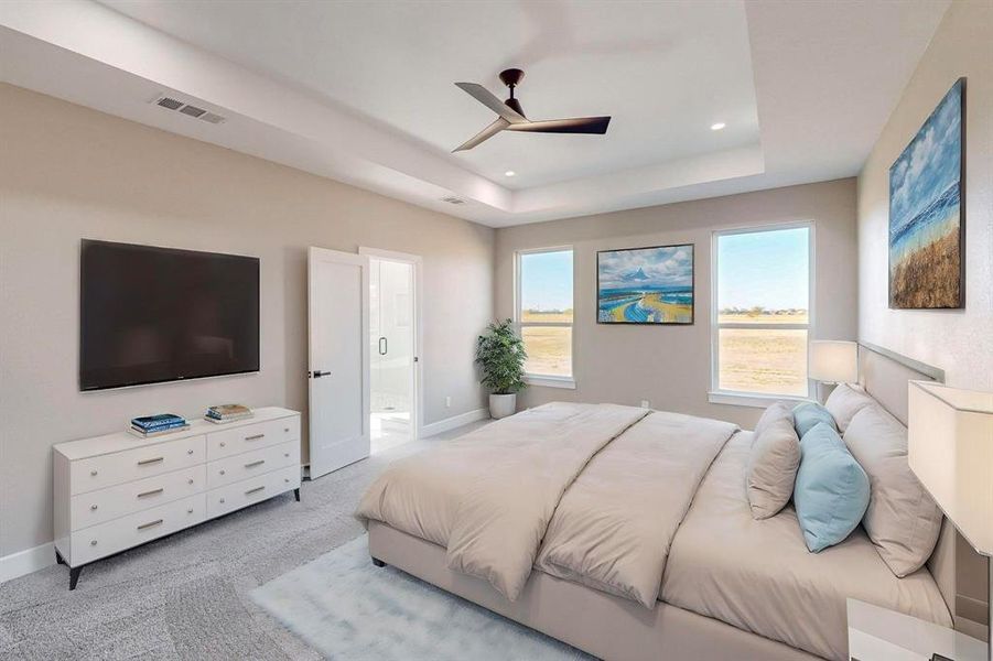 Carpeted bedroom with connected bathroom, ceiling fan, a raised ceiling, and multiple windows