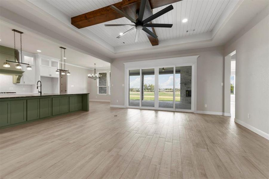 Unfurnished living room featuring ceiling fan with notable chandelier, sink, a tray ceiling, light hardwood / wood-style floors, and wood ceiling