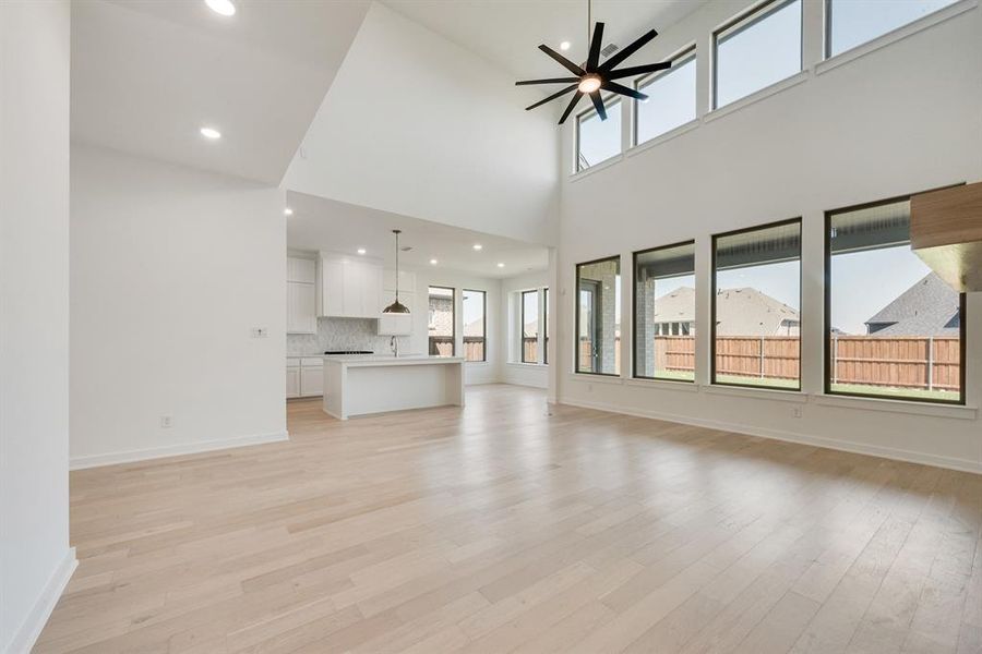 Unfurnished living room with recessed lighting, light wood-style flooring, a ceiling fan, and a high ceiling Unfurnished living room with recessed lighting, light wood-style flooring, a ceiling fan, and a high ceiling