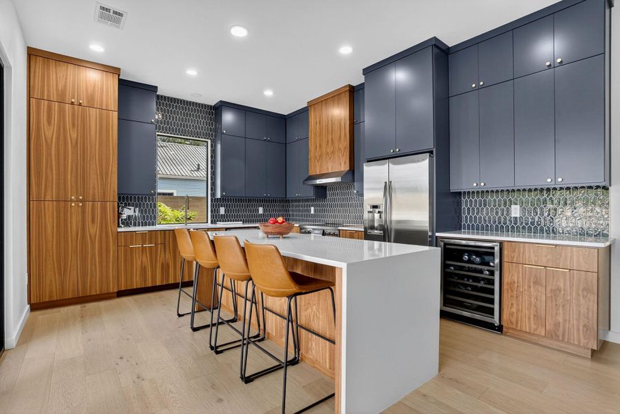 Kitchen with a breakfast bar area, a kitchen island, beverage cooler, modern cabinets, and light wood-type flooring