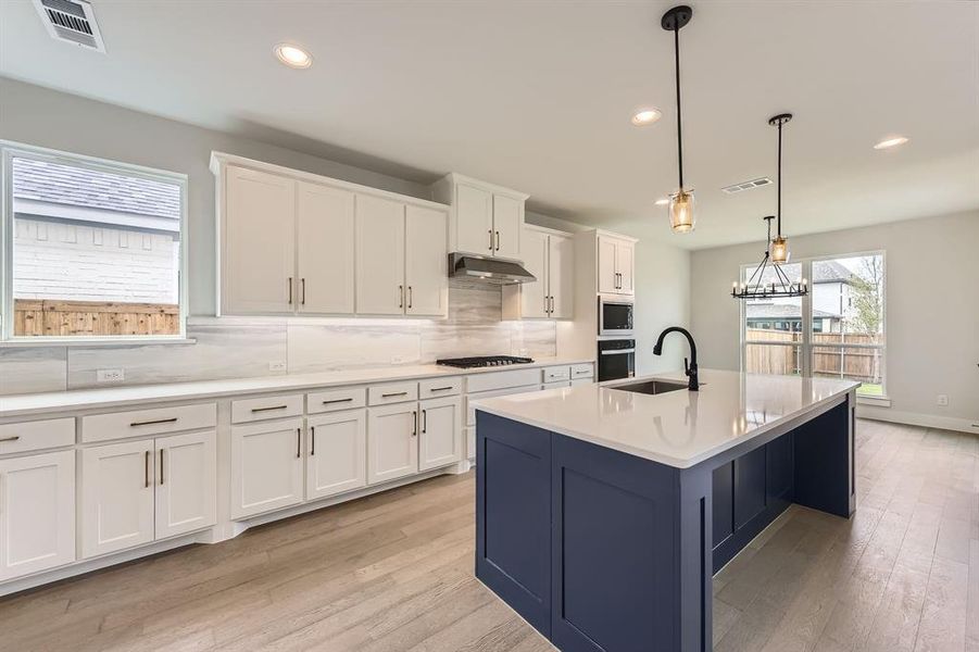 Kitchen with a sink, under cabinet range hood, stainless steel gas stovetop, white cabinets, and decorative backsplash