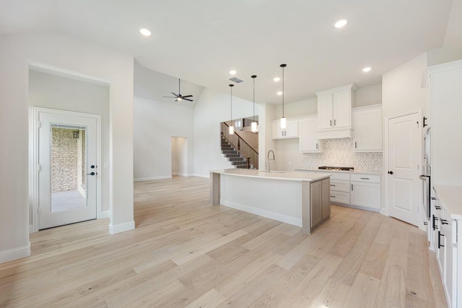 Open-concept kitchen with white cabinets, center island, and light hardwood floors open to living area with staircase Open-concept kitchen with white cabinets, center island, and light hardwood floors open to living area with staircase