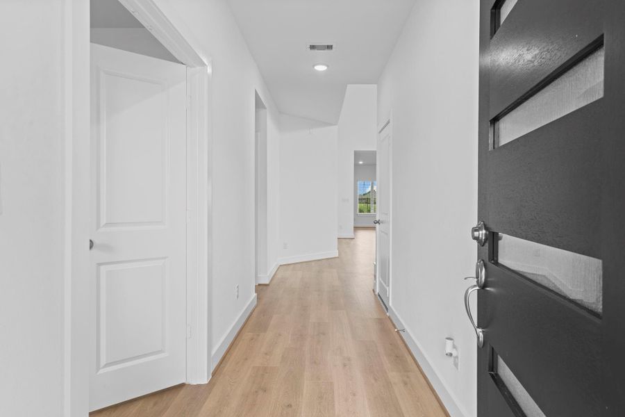 Step inside through the bold modern front door to a light-filled entry hallway featuring elegant wood-like tile flooring, and recessed lighting—setting a welcoming tone as it guides you toward the heart of the home with a glimpse of the living area and backyard view just ahead. **Image Representative of Plan Only and May Vary as Built**.