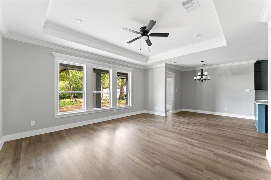Unfurnished living room with a tray ceiling, a chandelier, crown molding, ceiling fan, and light wood-style flooring