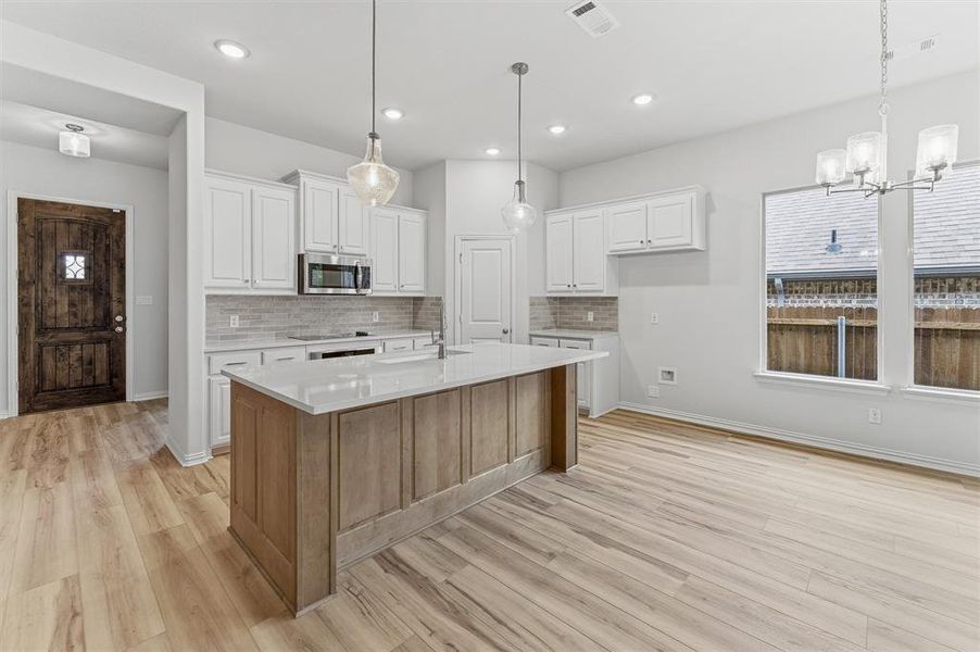 Open-concept kitchen featuring an island with a light wood-finish base, white countertops, stainless steel appliances, white cabinetry, and light wood-finish flooring