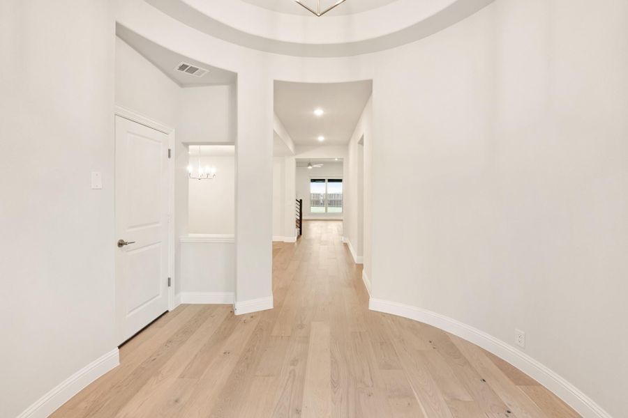 Curved entryway hallway with white walls, light hardwood floors, and round tray ceiling leading to main living area.