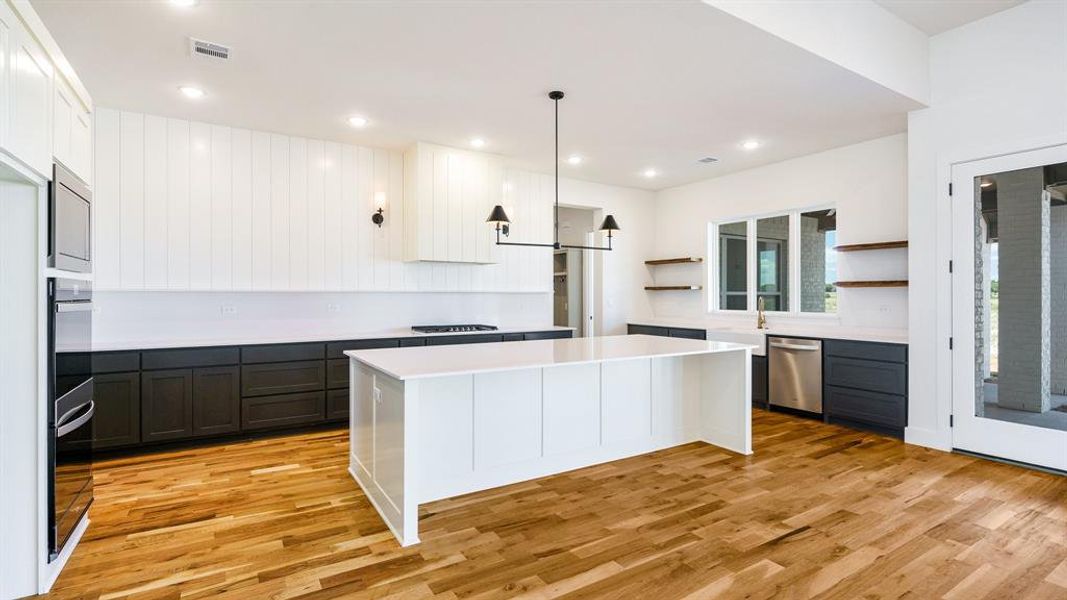 Kitchen featuring light hardwood / wood-style flooring, stainless steel appliances, white cabinetry, a center island, and pendant lighting