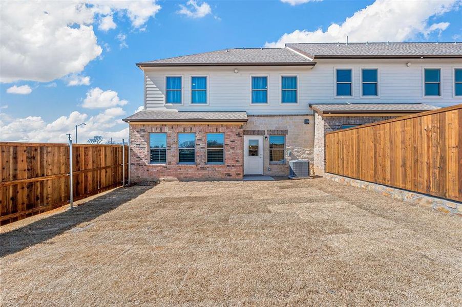 Rear view of house featuring a fenced backyard, a shingled roof, central AC, and brick siding