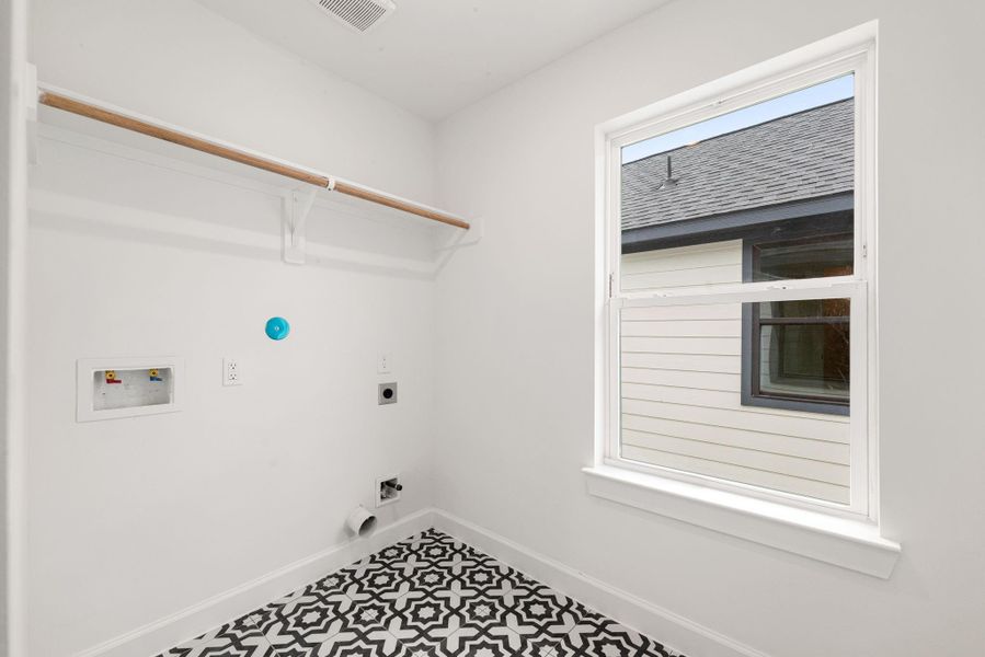 Dedicated laundry room featuring washer and dryer connections, built-in hanging shelf, and a window providing natural light. Stylish patterned tile flooring and a clean, functional layout designed for everyday convenience.