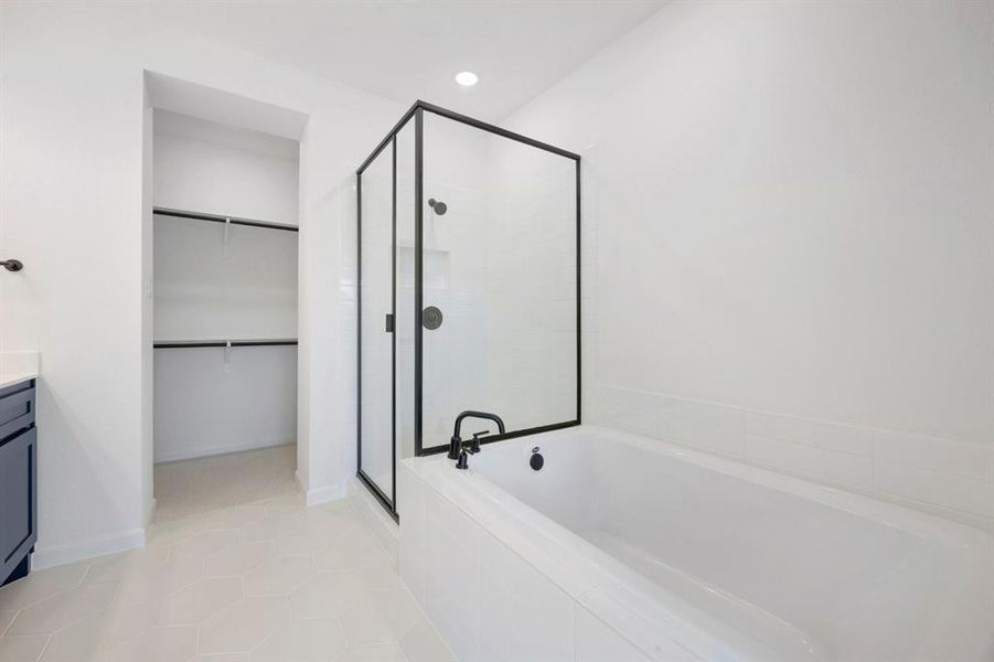 White bathroom featuring a built-in tub, separate shower with black-framed glass enclosure, dark vanity, and an open closet with shelving