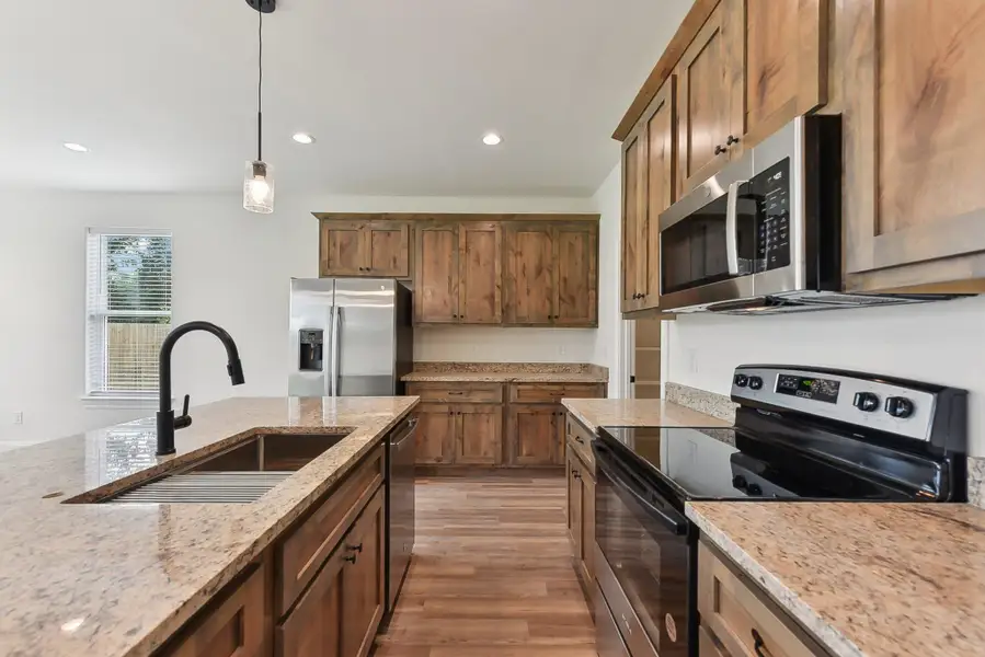 Kitchen featuring stainless steel appliances, a sink, light wood-style floors, light stone countertops, and pendant lighting