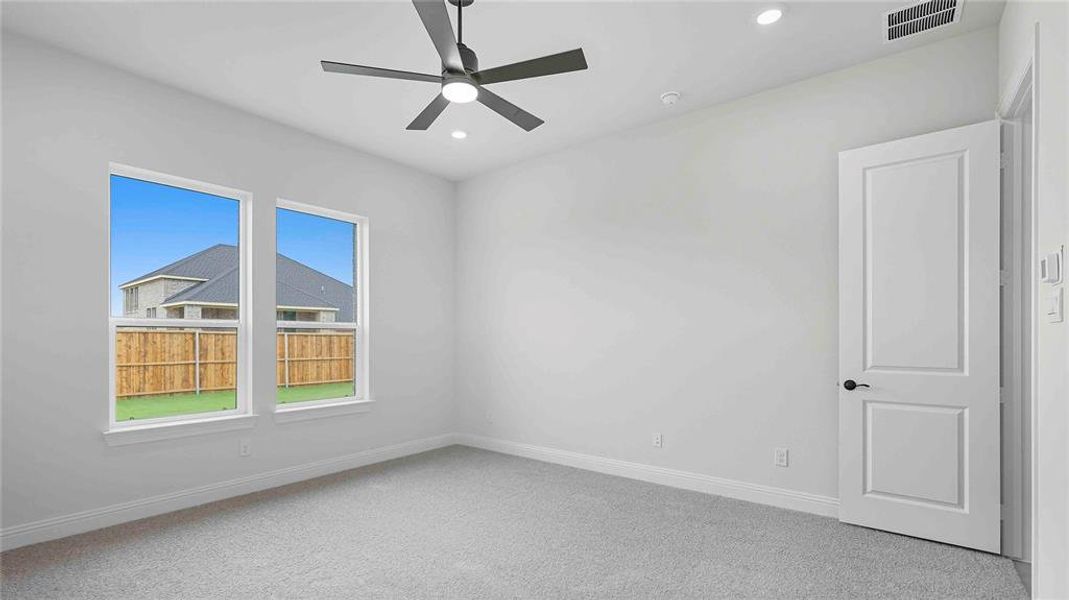Light grey carpeted room featuring two white-framed windows, a modern ceiling fan, recessed lighting, and a paneled interior door with matte black hardware