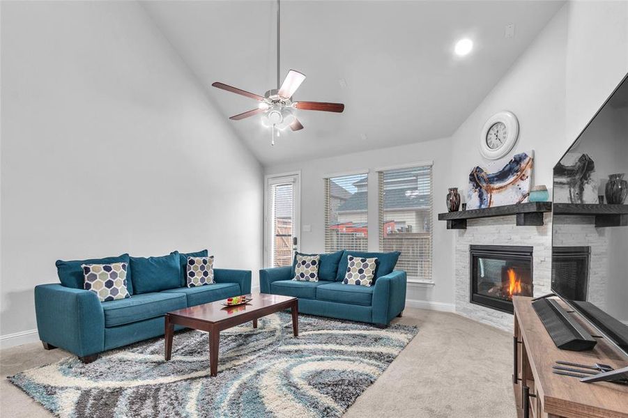 Living area with a fireplace, light colored carpet, ceiling fan, high vaulted ceiling, and baseboards