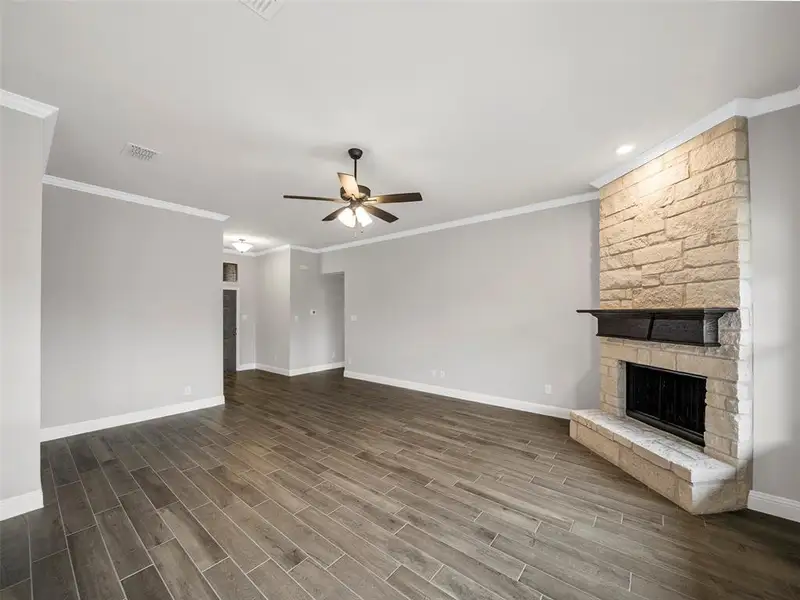 Unfurnished living room featuring a ceiling fan, a stone fireplace, baseboards, dark wood-style flooring, and visible vents