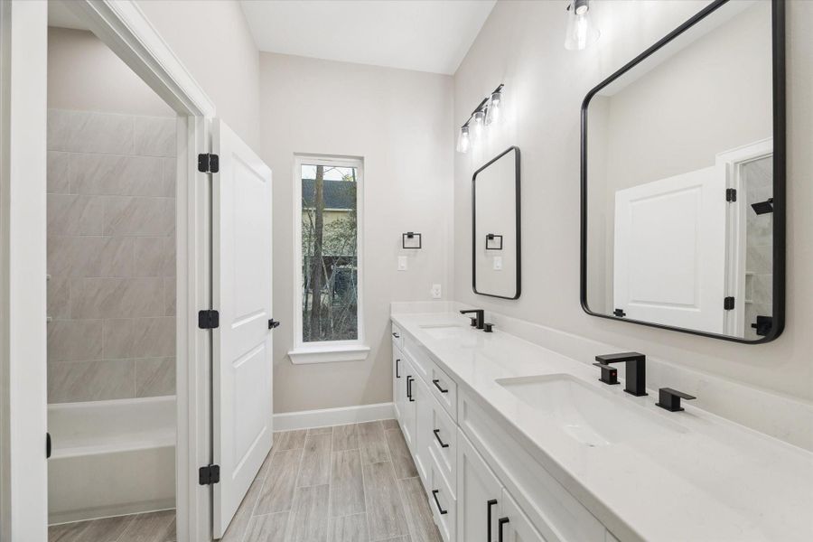 Secondary bathroom with separate potty room.  Long quartz counter with double sinks and framed mirrors.  Long window brings in natural light and looks to the side of the home.  Potty room with combination bath and shower.